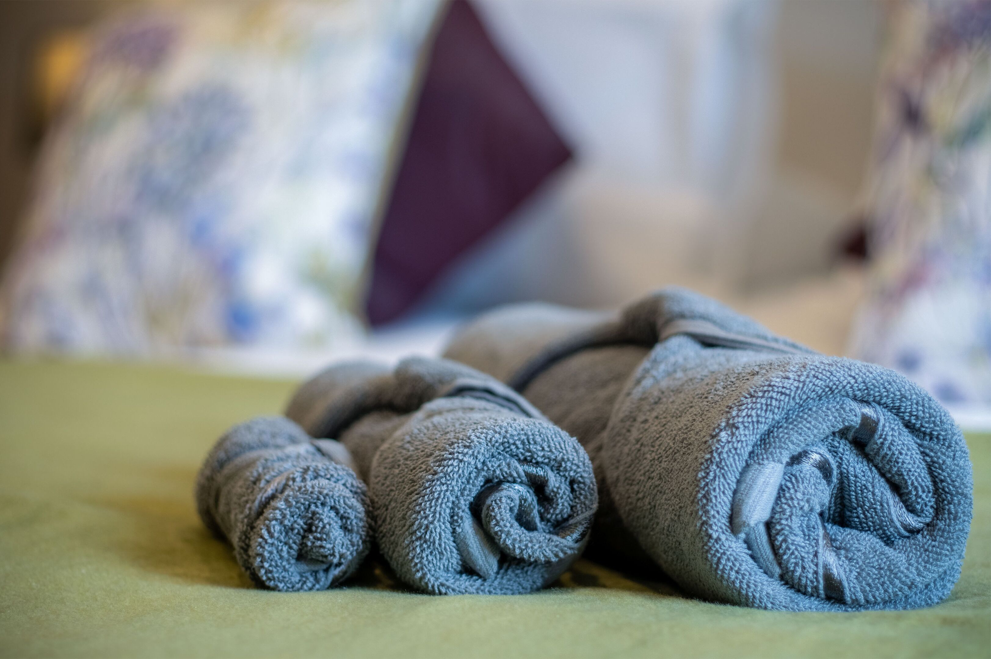 Ein Bett mit aufgerollten grauen Handtüchern und einer grünen Bettdecke.