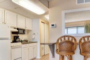 A kitchen with white cabinets, a microwave, a coffee maker, and two wicker chairs. - OC MD Direct Oceanfront Efficiency with pool parking gym White Marlin Open Week (Ocean City)