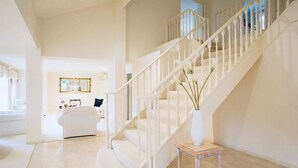 A spacious, well-lit interior with a white staircase, a white sofa, and a vase on a small table. - Sarovar Holidays (Traralgon)