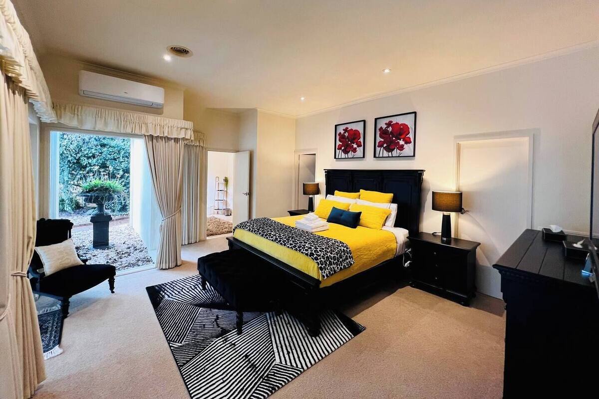 A spacious bedroom with a large bed, a sitting area with a chair, and a view of a garden through a sliding door.