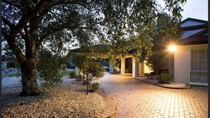 A paved pathway leading to a building with a covered entrance, surrounded by trees and gravel landscaping. - Sarovar Holidays (Traralgon)