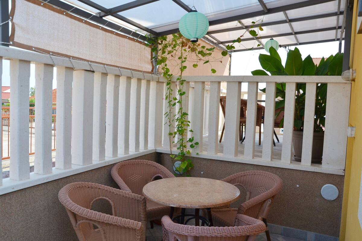 A covered patio with wicker furniture, a round table, and a white picket fence.