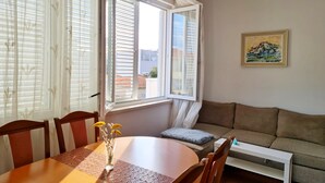 Une pièce comprenant une table à manger, des chaises, un canapé, un radiateur et une fenêtre avec des stores.