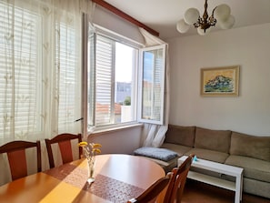 A room with a dining table, chairs, a sofa, a radiator, and a window with blinds. - Apartments Damjanka (Orebic)