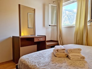 A bedroom with a bed, a bedside table with a lamp, a mirror, and a window with curtains. - Apartments Damjanka (Orebic)