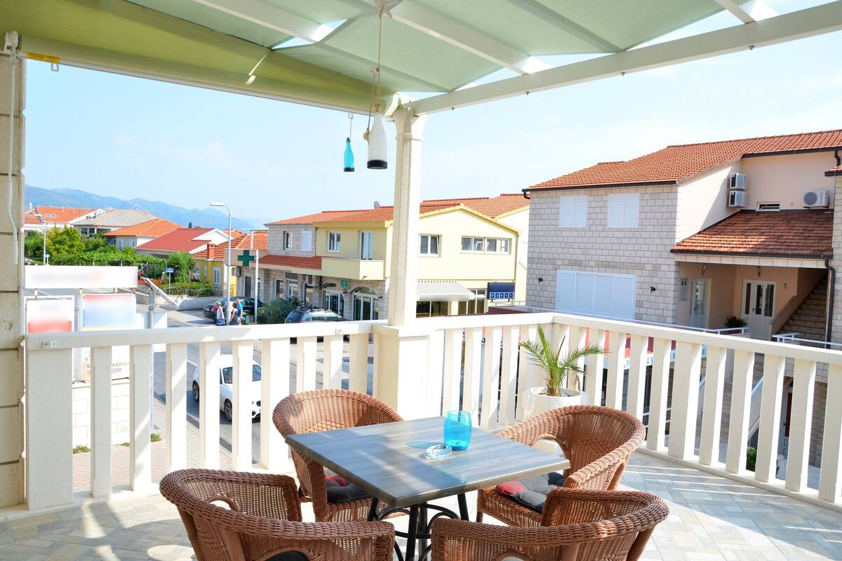 A balcony with wicker furniture, a table, and a view of buildings and a street.