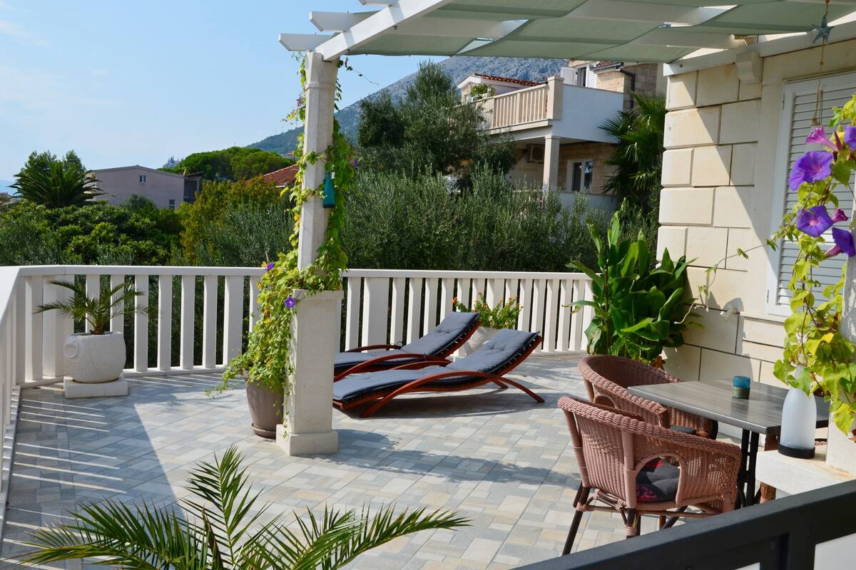 A balcony with two lounge chairs, a table, and potted plants.