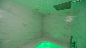 A bathroom with a green-lit jacuzzi, marble walls, and a showerhead. - Villa Yael eilat (Eilat)