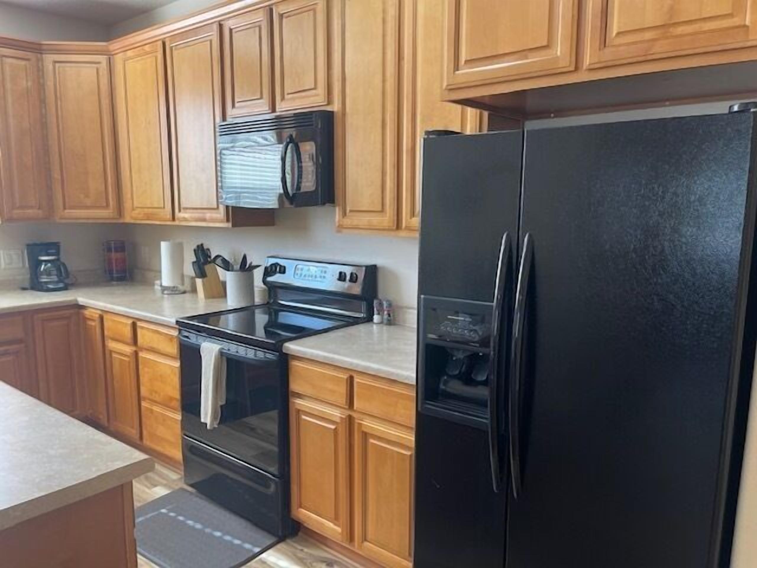 A kitchen with wooden cabinets, a black refrigerator, a stove, and a coffee maker.