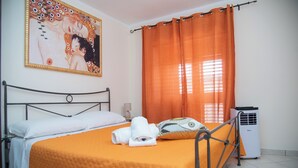 Une chambre d’hôtel avec un lit, des rideaux orange, un radiateur et un tableau au mur.