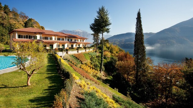 A large house with a swimming pool, surrounded by a well-maintained garden and a view of mountains and a lake.