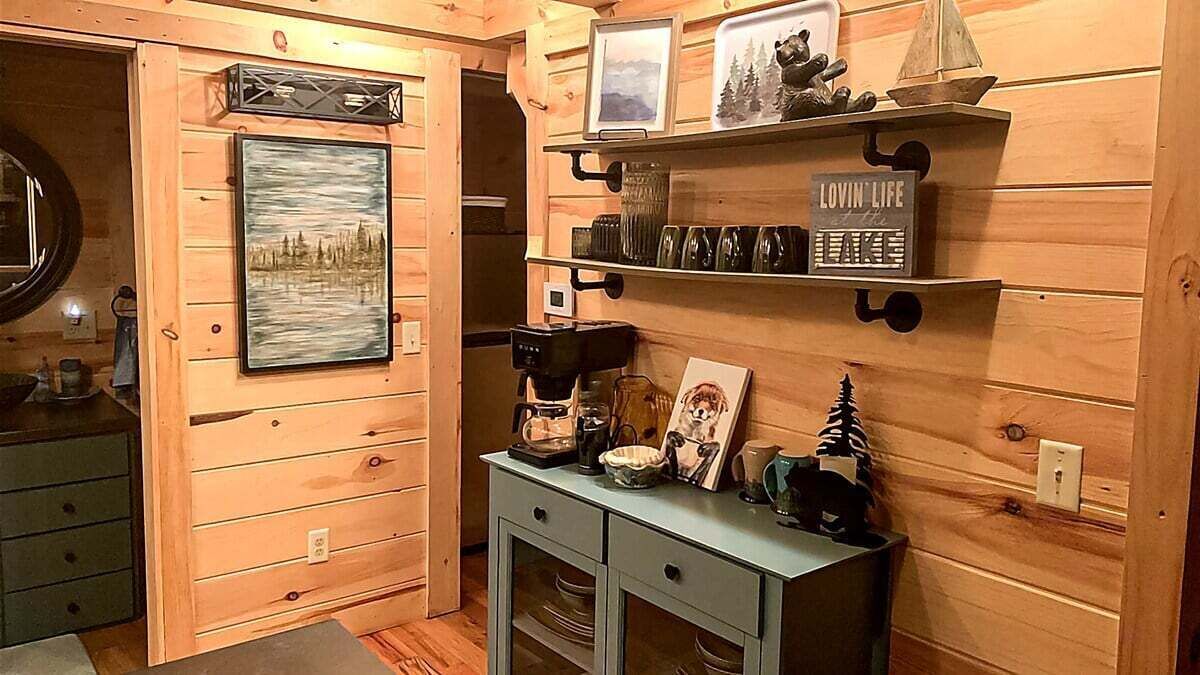 Een houten interieur met een lijstfoto, planken met decoratieve objecten, een koffiezetapparaat en een klein kastje.
