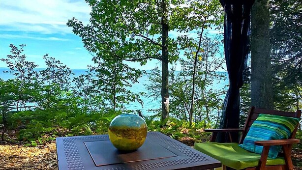 Ein Tisch mit einer Glasvase, ein Sessel mit Kissen und Blick auf Meer und Bäume.