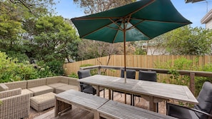 An outdoor patio with a wooden table and chairs, a wicker sofa, and a green umbrella.