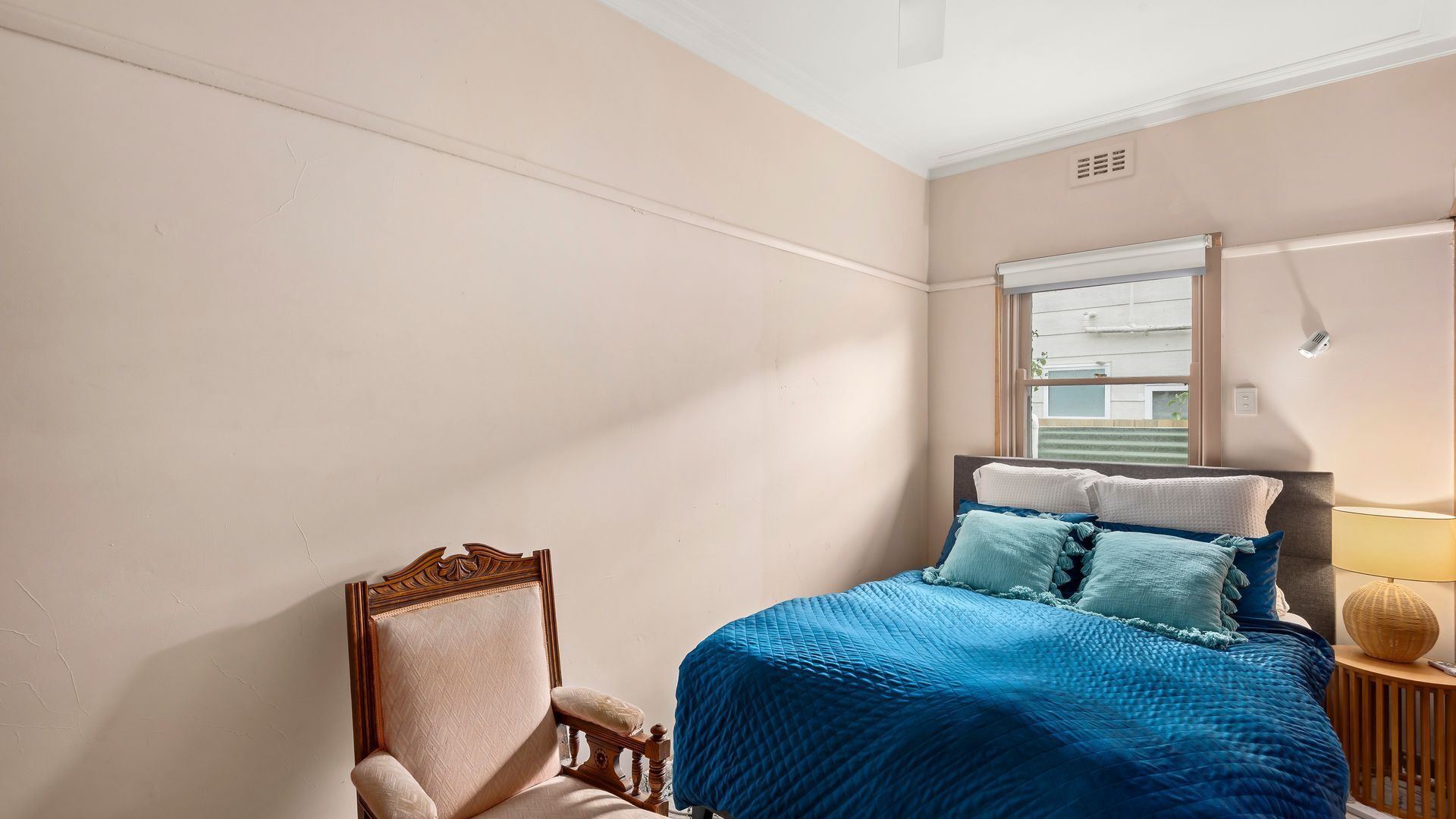 A bedroom with a bed, a chair, a window, and a lamp.