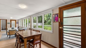 A dining area with a wooden table and chairs, large windows, and a door with frosted glass panels.