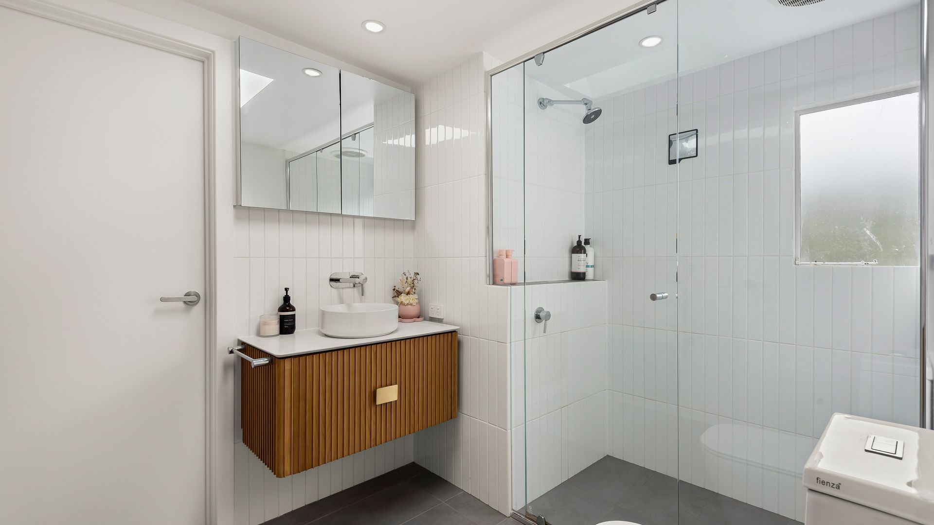 Une salle de bain moderne avec une douche à parois de verre, un meuble-lavabo en bois et un lavabo blanc.