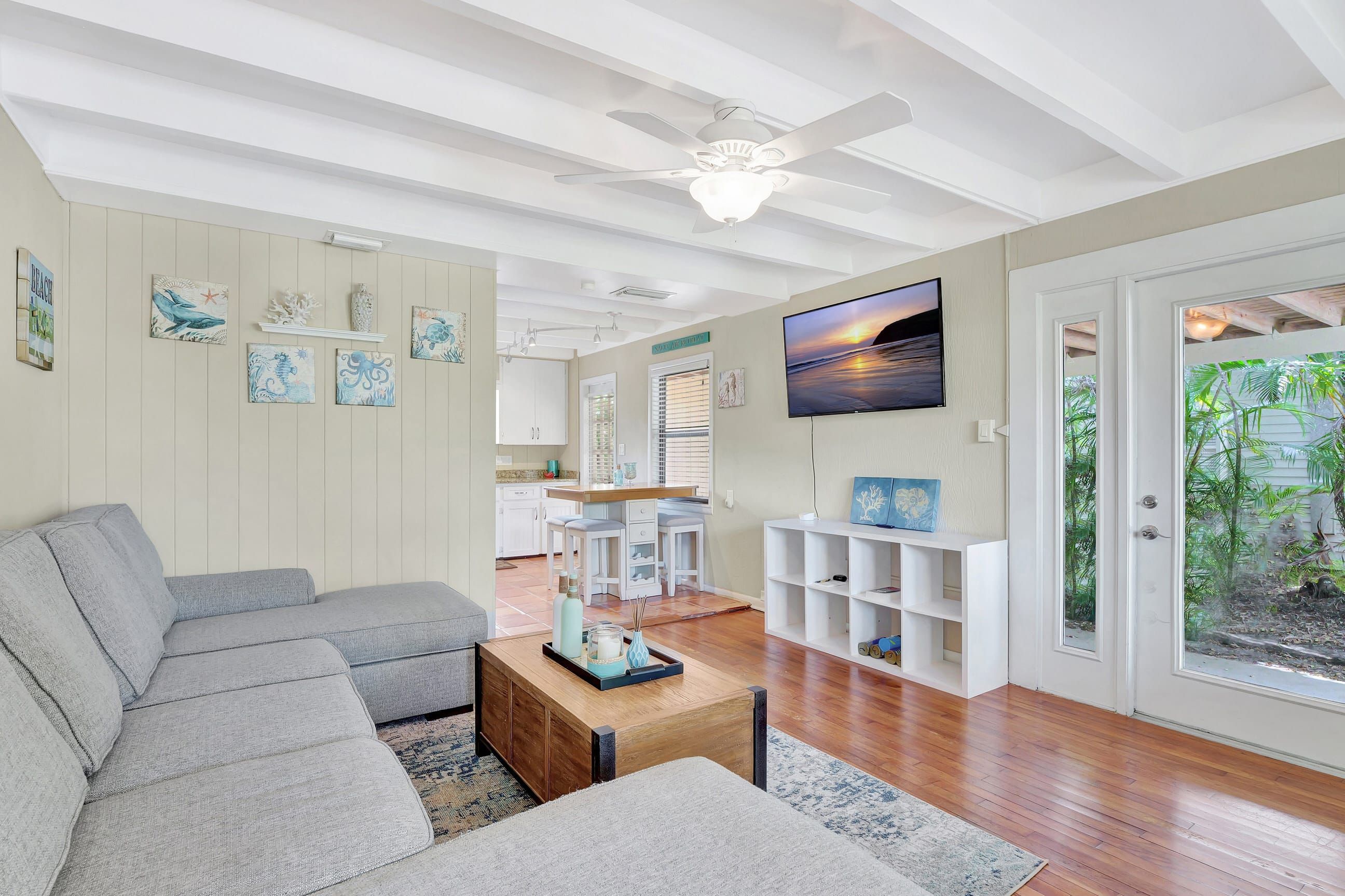 A modern living room with a grey sectional sofa, a wooden coffee table, and a TV mounted on the wall.