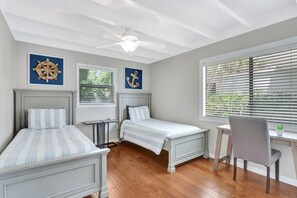 A bedroom with two beds, a desk, and a chair. There are ceiling fans and artwork on the walls.