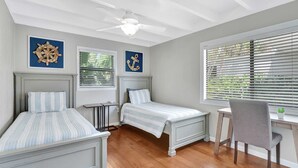 Une chambre avec deux lits, un bureau et une chaise. Il y a des ventilateurs de plafond et des œuvres d’art accrochées aux murs.