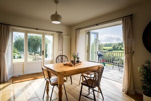 A dining area with a wooden table and chairs, large windows, and a view of the outdoors. - Luxury bolthole in secluded valley near coast (AXMINSTER)