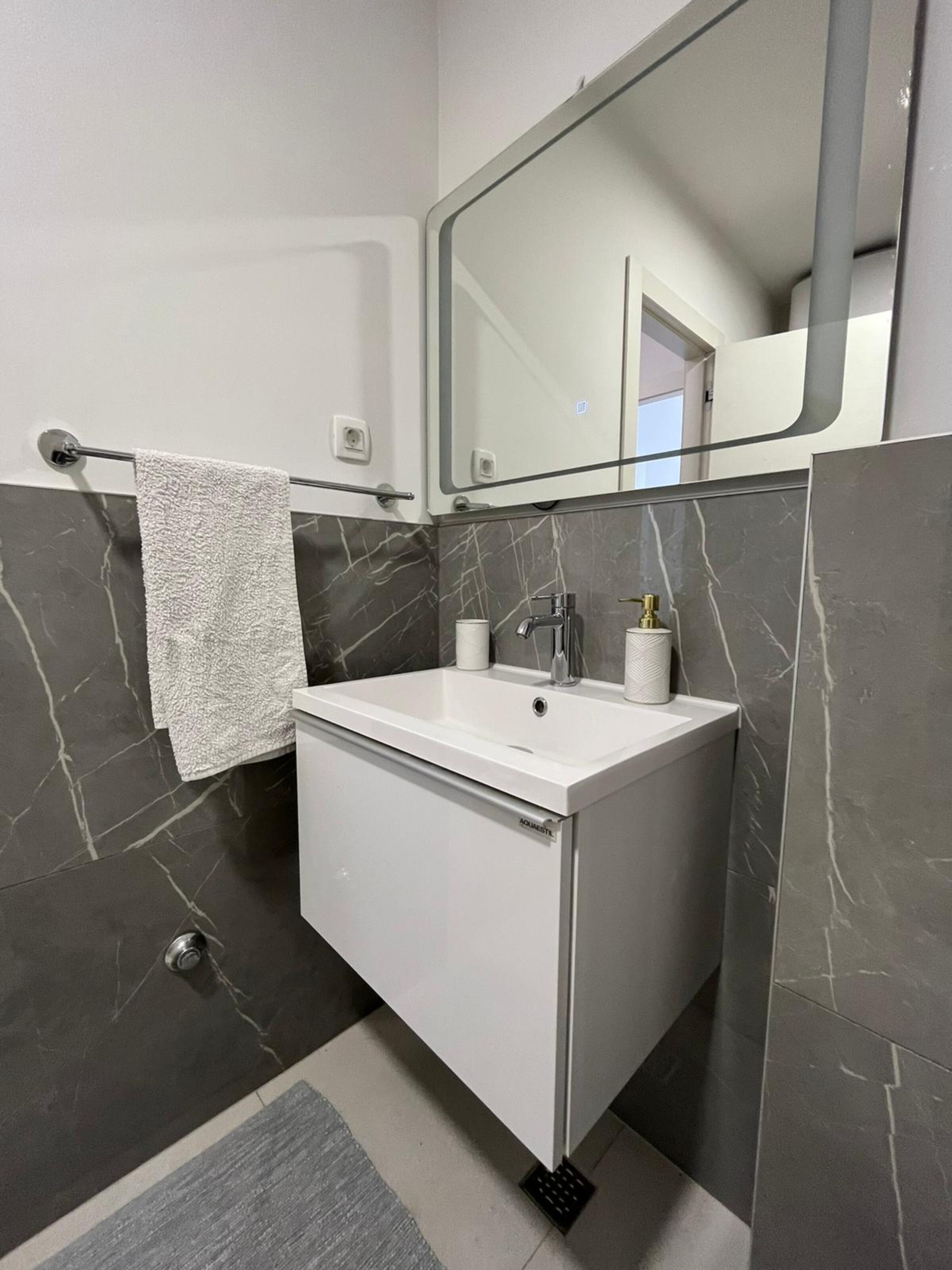 A modern bathroom with a white sink, marble walls, a towel rack, and a large mirror.
