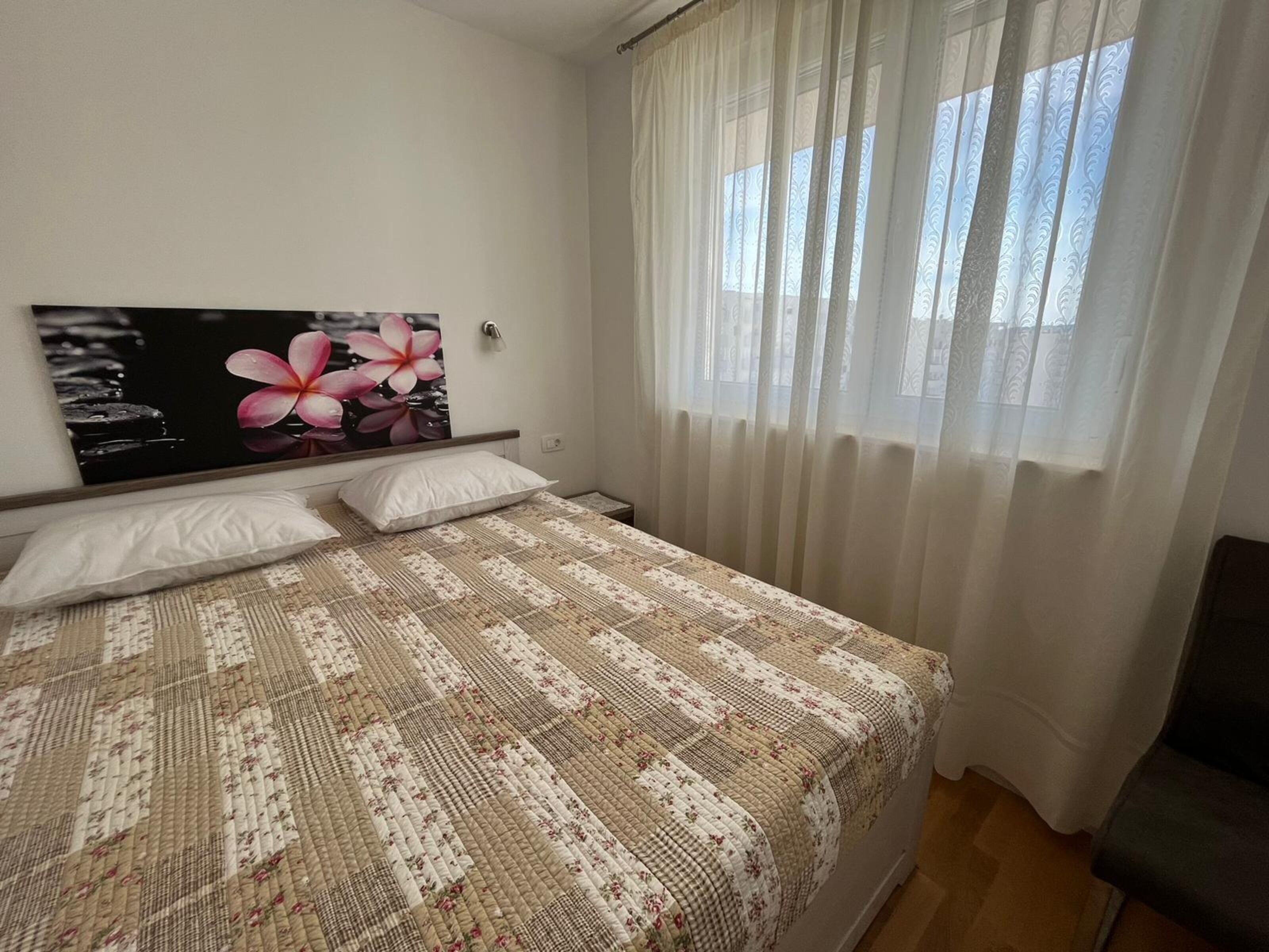 A bedroom with a bed, a wall-mounted artwork, and a window with sheer curtains.