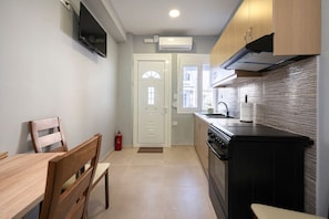 A compact kitchen with a dining area, a TV mounted on the wall, and a door leading to another room.