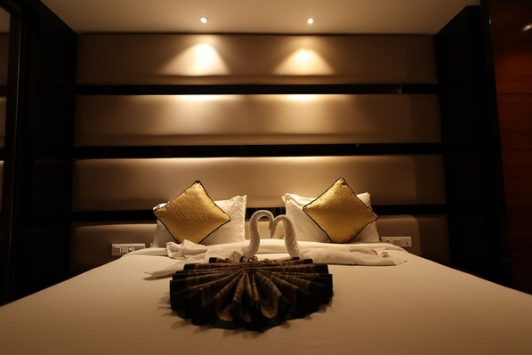 A hotel room with a neatly made bed, two golden pillows, and a swan-shaped towel arrangement.
