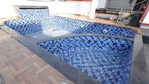 A swimming pool with a blue mosaic tile design, surrounded by a wooden deck and a concrete border. - THE LATITUDE LUXURY  (Haridwar)