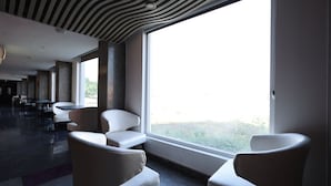 A modern interior with large windows, seating areas, and a patterned ceiling. - THE LATITUDE LUXURY  (Haridwar)