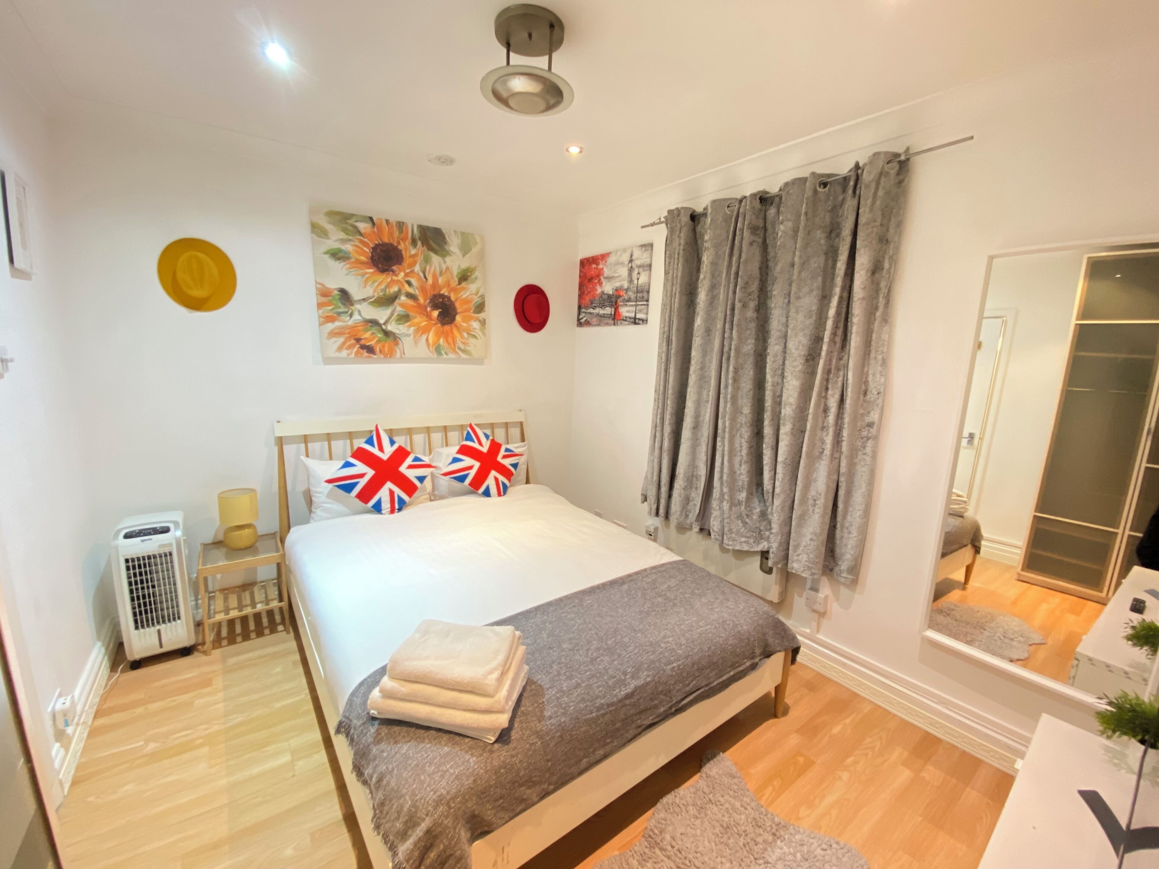 A bedroom with a bed, a bedside table, a lamp, a wall clock, a painting, a mirror, and a wardrobe.