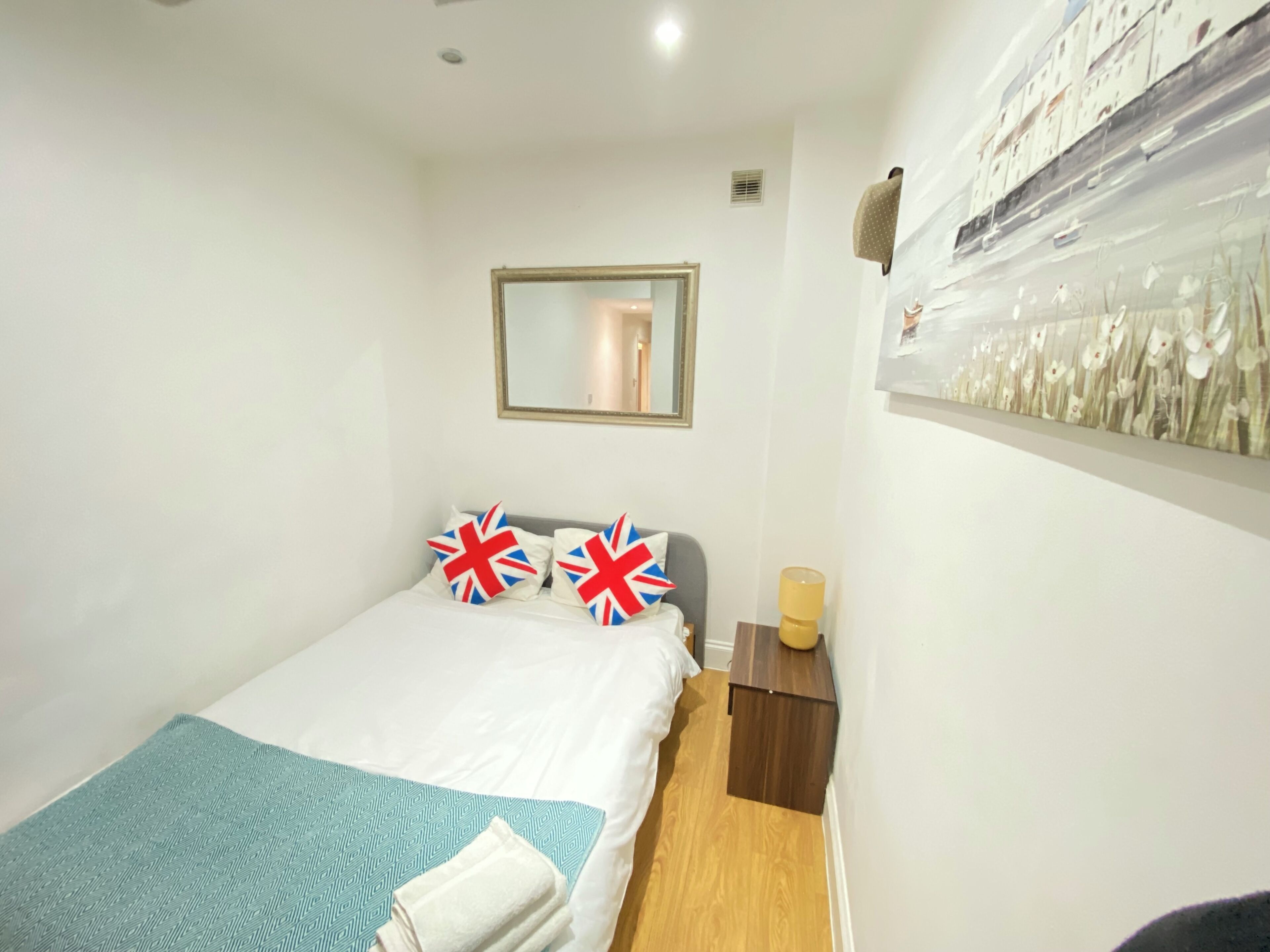 Ein Schlafzimmer mit Bett, Nachttisch, Spiegel und Wandbild.
