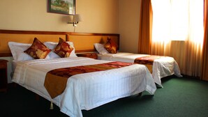 Habitació d'hotel amb dos llits, una tauleta de nit, una làmpada, un quadre i una finestra amb cortines.