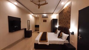 A hotel room with a bed, a ceiling fan, a TV, and a wall-mounted air conditioner. - THE PALMS RESORT (Rishikesh)