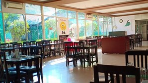 A spacious dining area with large windows, wooden tables, and chairs. - THE PALMS RESORT (Rishikesh)