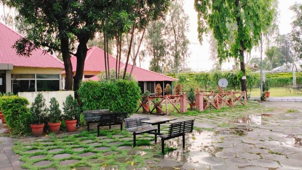A courtyard with a red-roofed building, potted plants, and a bench. - THE PALMS RESORT (Rishikesh)