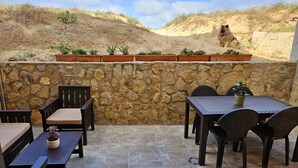 Eine Terrass mit Steinmauern, Steinboden und einem Tisch mit Stühlen.