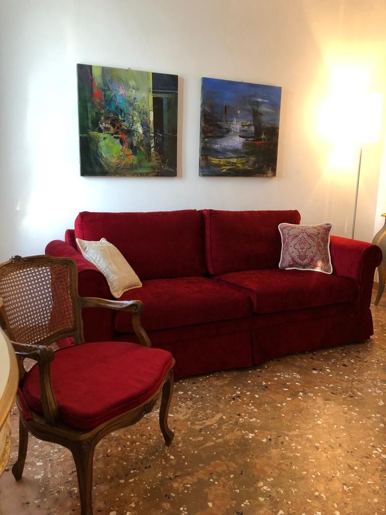 A red sofa with two cushions, a wooden chair, and two abstract paintings on the wall.