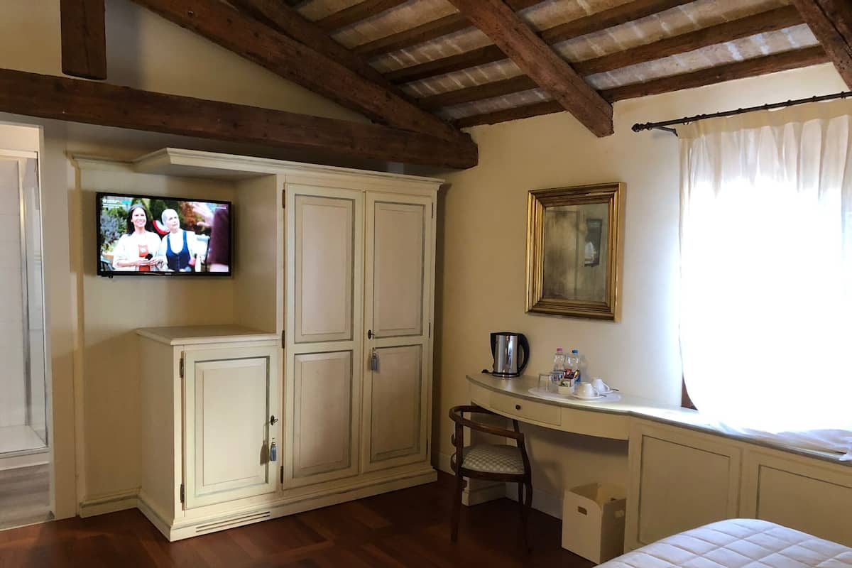 Una habitación con techo de madera, un televisor en la pared, un escritorio con silla, una cama y una ventana con cortinas.