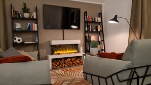 A modern living room with a fireplace, a flat-screen TV, and bookshelves. - Penthouse in Waterfront Villa Including Wifi Parking Balcony Netflix (Wildau)