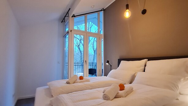 A hotel room with two beds, a large window, and a ceiling light fixture. - Penthouse in Waterfront Villa Including Wifi Parking Balcony Netflix (Wildau)