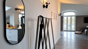 A modern interior with a large mirror, a black umbrella on a stand, and a dining area in the background. - Penthouse in Waterfront Villa Including Wifi Parking Balcony Netflix (Wildau)