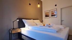 A modern bedroom with a large bed, a bedside table, a lamp, and two wall-mounted light fixtures. - Penthouse in Waterfront Villa Including Wifi Parking Balcony Netflix (Wildau)