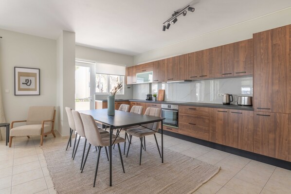 A modern kitchen with wooden cabinets, a dining area with a table and chairs, and a large window providing natural light.