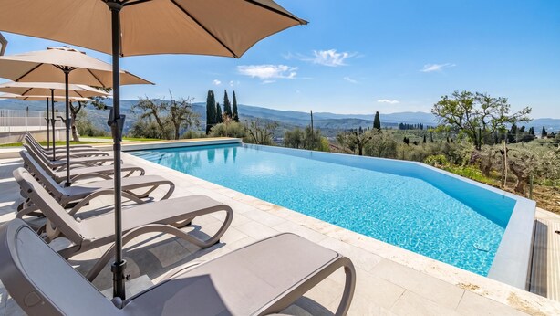 A swimming pool with lounge chairs and umbrellas, surrounded by trees and a view of distant mountains. - Amazing Villa Chimera White View Pool (Arezzo)