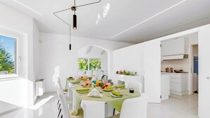 A modern dining area with a table set for four, white chairs, and a view of the outdoors. - Amazing Villa Chimera White View Pool (Arezzo)