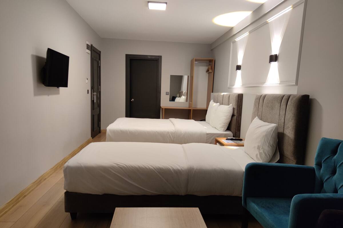A hotel room with two single beds, a sofa, a TV, and a mirror.