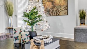 Een woonkamer met een witte kerstboom, een kamerplant, een boek en decoratieve objecten op een houten tafel.