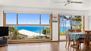 Ein Zimmer mit einem großen Fenster und Meerblick, sowie einem Balkon mit Tisch und Stühlen.